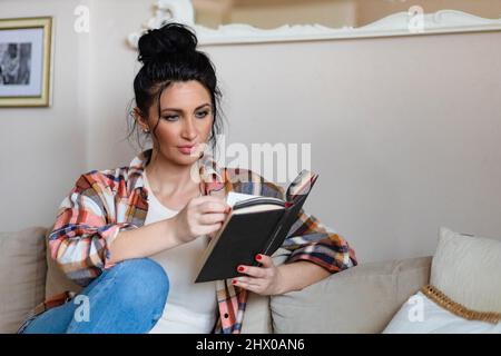 Blauäugige Frau mittleren Alters, die ein Buch liest Stockfoto