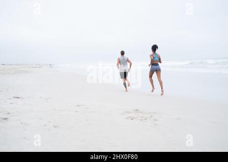 Ihre Strandkörpern für den Sommer vorbereiten. Rückansicht eines jungen Paares, das zusammen am Strand entlang läuft. Stockfoto