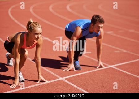 Ich nehme dich auf. Aufnahme von zwei jungen Menschen, die sich auf eine Leichtathletik-Rennstrecke vorbereiten. Stockfoto