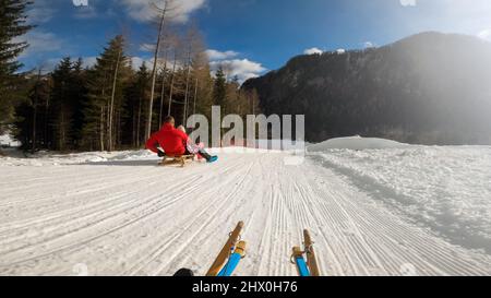 Sicht auf ein Kinderrodeln mit Vater und Schwester, auf einem Holzschlitten auf dem Hügel am sonnigen klaren Wintertag. Stockfoto