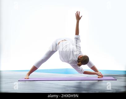 Zeigt eine perfekte Dreieckshaltung. Aufnahme einer wunderschönen jungen Frau, die im Freien neben einem Pool Yoga macht. Stockfoto
