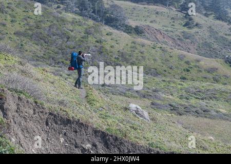 Ein Backpacker auf einer Wanderung macht Halt, um mit einem Teleobjektiv am Lost Coast Trail im Humboldt County, Nordkalifornien, USA, Fotos zu machen. Stockfoto