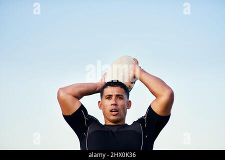 Suche nach meinen Teamkollegen. Kurzer Schuss eines hübschen jungen Sportlers, der alleine steht und während des Trainings einen Rugby-Ball wirft. Stockfoto