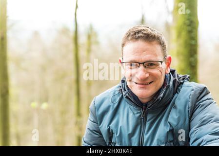 Kordel, Rheinland-Pfalz - Deutschland - 04 13 2019 - Nahaufnahme eines 40-jährigen, weiß lächelnden Mannes mit Brille und blauer jacke zur Saisonmitte Stockfoto