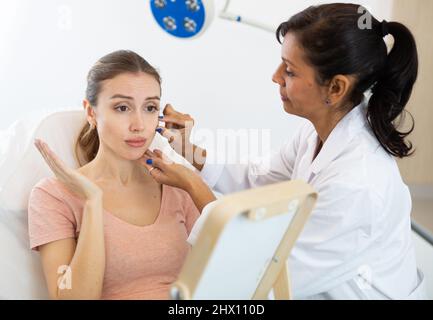 Junge Frau, die während der Untersuchung des Kosmetologen den Spiegel hält Stockfoto