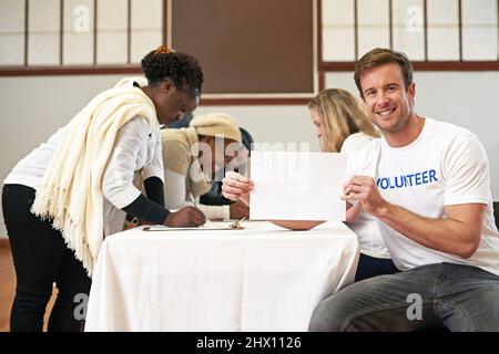 Es ist perfekt für Ihre Nächstenliebe. Beschnittenes Porträt eines Freiwilligen mit leerem Schild, während Freiwillige Unterschriften im Hintergrund erhalten. Stockfoto