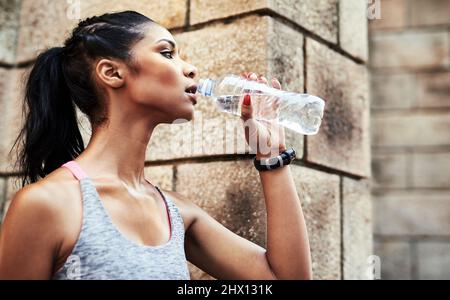 Den Durst löschen. Aufnahme einer attraktiven jungen Sportlerin, die beim Training im Freien Wasser aus einer Flasche trinkt. Stockfoto