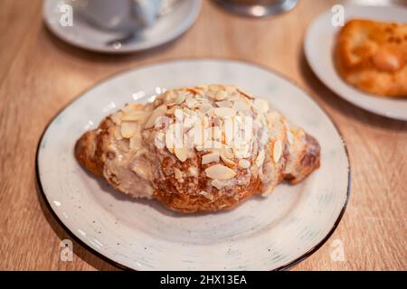 Ein frisches großes Croissant auf einem schönen Teller in einem Café oder Restaurant. Nahaufnahme eines Croissants und einer mit Nüssen bestreuten Creme. Süßes und köstliches Dessin Stockfoto