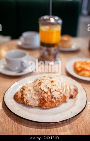 Ein frisches großes Croissant auf einem schönen Teller in einem Café oder Restaurant. Nahaufnahme eines Croissants und einer mit Nüssen bestreuten Creme. Süßes und köstliches Dessin Stockfoto