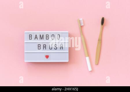 Zwei natürliche, umweltfreundliche Bambusbürsten mit weißen und schwarzen Borsten und Lightbox-Text Bambus-Pinsel auf papierrosafarbenem Hintergrund. Draufsicht Flat Lay Templ Stockfoto