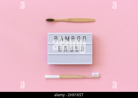 Zwei natürliche, umweltfreundliche Bambusbürsten mit weißen und schwarzen Borsten und Lightbox-Text Bambus-Pinsel auf papierrosafarbenem Hintergrund. Draufsicht Flat Lay Templ Stockfoto