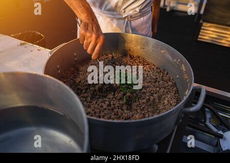 Nahaufnahme eines von Hand gerührenden Küchenchefs aus gemahlenem Rindfleisch mit Oregano Stockfoto