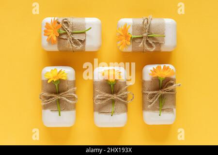 Handgemachte Naturseife, verziert mit Bastelpapier, Geißeln und orangefarbenen Ringelblumenblumen auf gelbem Hintergrund. Bio-Kosmetik, Null Abfall, Öko Fr. Stockfoto