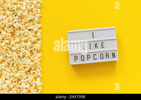 Verstreute Popcorn-Bordüre am linken Rand und Leuchtkasten-Text Ich mag Popcorn auf gelbem Papierhintergrund. Vorlage in der Draufsicht. Stockfoto