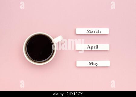 Holzkalender Frühlingsmonate März April Mai und Tasse schwarzen Kaffee auf pastellrosa Papier Hintergrund gerichtet März. Konzept Hallo März Kreativ Stockfoto