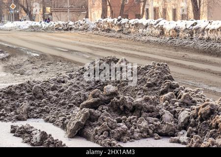 Haufen schmutzigen Schnees auf den Straßen der Stadt in Sibirien. Sand und Reagenzien gegen Eisglätte. Stockfoto