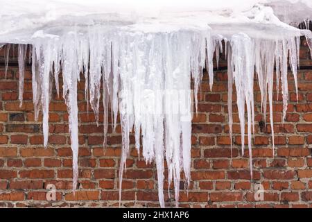 Eiszapfen, die vom Dach des Gebäudes hängen. Große Eiszapfen und Eisblöcke beim Sturz vom Dach stellen eine Lebensgefahr für die Menschen dar. Stockfoto