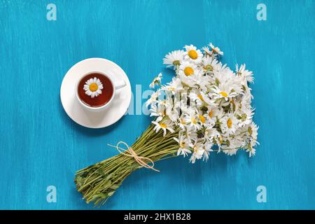 Blumenstrauß Feld Chamomies Tasse Kräutertee auf blauem Holzhintergrund, Rustikale Vintage-Stil, Konzept Guten Morgen Sommer Teatime Tea Party flach Stockfoto