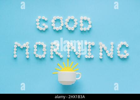 Text Guten Morgen von Marschmalow und Kaffeetasse mit gelb aufgehender Sonne auf blauem Hintergrund. Konzept Grußkarte von oben Stockfoto