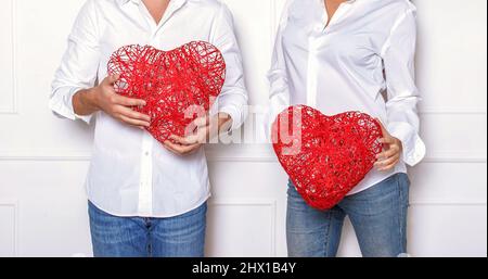 Mann und Frau in einem weißen Hemd und einer blauen Jeans mit roten Korbherzen. Romantische Fotosession im Studio am Valentinstag. Stockfoto