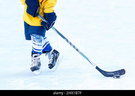 Füße eines jungen Eishockeyspielers, Hockeyschläger und Puck Nahaufnahme auf dem Hintergrund des Eises. Stockfoto