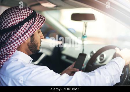 Sie haben Ihr Ziel erreicht. Aufnahme eines jungen muslimischen Geschäftsmannes, der sein Telefon benutzte, während er ein Auto fuhr. Stockfoto