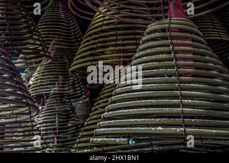 Mehrere große gelbe Räucherstäbchen hängen in Stapeln an der Decke in einem chinesischen Schrein. Große glockenförmige Spiral-Räucherstäbchen, Fokus und Unschärfe. Stockfoto