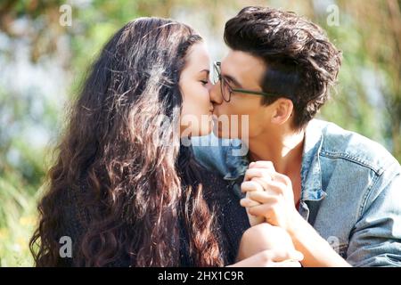 Einen intimen Kuss teilen. Nettes junges Paar, das draußen sitzt und einen romantischen Kuss teilt. Stockfoto