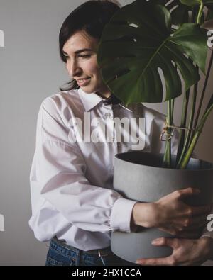 Die junge Frau steht mit einem großen Blumentopf mit Monstera Stockfoto
