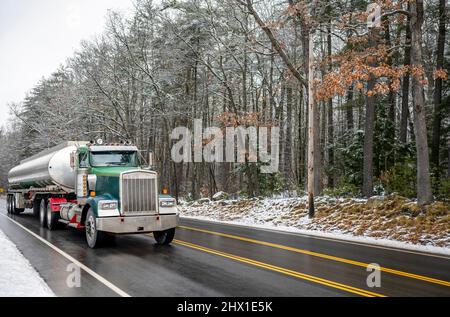 Industrial Green Day Cab Classic Motorhaube Big Rig Semi-Truck Transport von flüssigen Fracht in langen ovalen Zisterne Tank Sattelanhänger läuft auf den nassen Winter Stockfoto