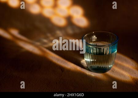 Blaue Glasvase mit Wasser auf sandfarbenem Hintergrund mit Licht und Schatten und Kopierraum geschnitzt Stockfoto