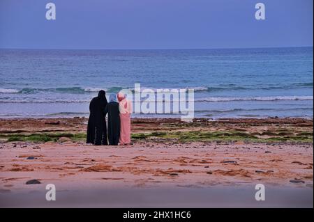 Rückansicht von drei Frauen in traditionell arabischer Kleidung am Sandstrand Stockfoto