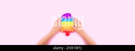 Banner mit Kinderhände halten farbige Pop it Anti-Stress-Spielzeug isoliert auf rosa Hintergrund. Nahaufnahme. Stockfoto
