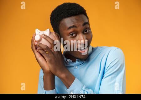 Junger afrikanischer amerikanischer Mann mit Sparschwein auf gelbem Hintergrund Stockfoto