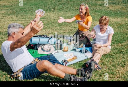 Älterer Mann, der feiert, dass er während eines Ausflugs seine Familie mit Spielkarten gewonnen hat Stockfoto