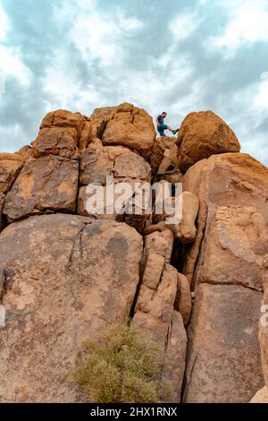 Junger Mann auf den Joshua Tree Felsen fühlt sich frei in der erstaunlichen Landschaft. Stockfoto