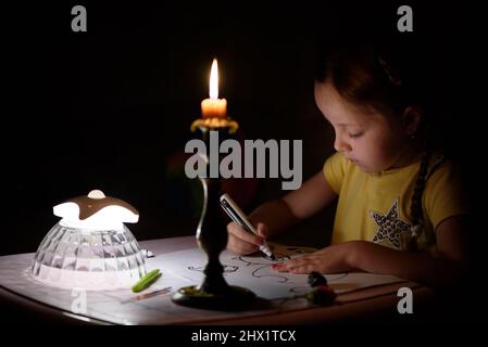 Das kleine Mädchen zieht in einem dunklen Raum Fantasiefiguren in die Nähe von Kerzen. Kind, das während eines Stromausfalls seine Lieblingssache macht. Stockfoto