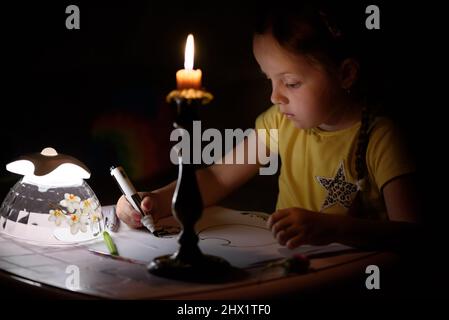 Das kleine Mädchen zieht in einem dunklen Raum Fantasiefiguren in die Nähe von Kerzen. Kind, das während eines Stromausfalls seine Lieblingssache macht. Stockfoto