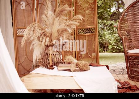 Böhmischer Boho-Stil der Garteneinrichtung. Tischdekor mit Vintage-Büchern und trockenem Schilf auf Leinentischdecken. Ästhetische Dekorationen für eine Hochzeit d Stockfoto