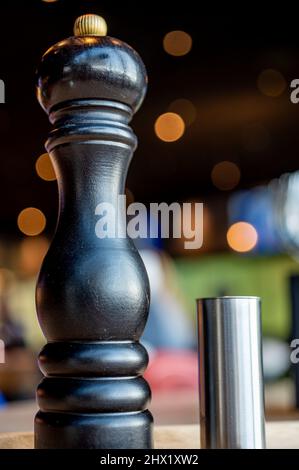 Salz- und Pfefferstreuer. Salz- und Pfeffertöpfe auf dem Tisch. Metallsalzkeller. Hölzerne Pfeffermühle. Stockfoto