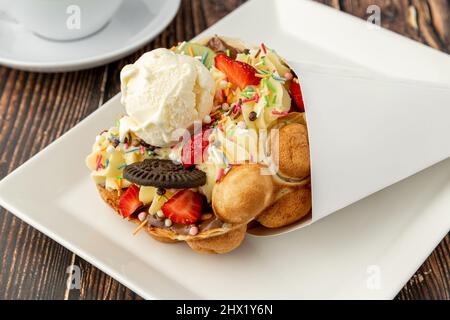 Hong kong oder Bubble Waffel mit Eis, Obst, Schokoladensauce und bunten Süßigkeiten Stockfoto