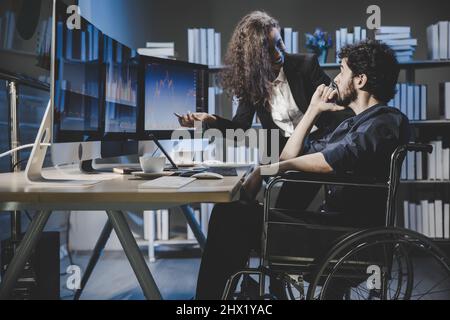 Teammarker sitzen auf dem Rollstuhl und schauen sich auf dem Monitor-Computer das Börsendiagramm an, um vor dem Angebot zu analysieren und Transaktionen zwischen Käufer und zu arrangieren Stockfoto