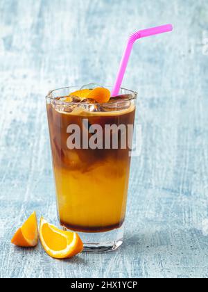Orangefarbener kalter Kaffee mit Eiswürfeln auf blauem Steinhintergrund Stockfoto