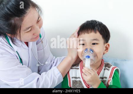 Glückliches Kind mit Atemwegserkrankung, das von einem Arzt mit Inhalator unterstützt wurde. Kinderarzt kümmern asiatischen Jungen mit Asthma Probleme machen Inhala Stockfoto