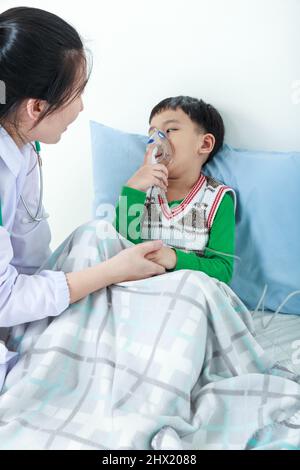 Glückliches Kind mit Atemwegserkrankung, das von einem Arzt mit Inhalator unterstützt wurde. Kinderarzt kümmern asiatischen Jungen mit Asthma Probleme machen Inhala Stockfoto