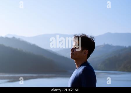 Asiatischer Mann lächelt und schaut mit Berg jeden See Hintergrund. Gutes Konzept für die psychische Gesundheit. Stockfoto