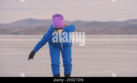 Das Mädchen trainiert auf Eisschnelllauf. Das Kind Schlittschuhe im Winter in blauem Sportswear-Anzug, Sportbrille. Kinder Eisschnelllauf Sport. Zeitlupe im Freien. Schneebedeckte Berge, schönes Eis. Stockfoto