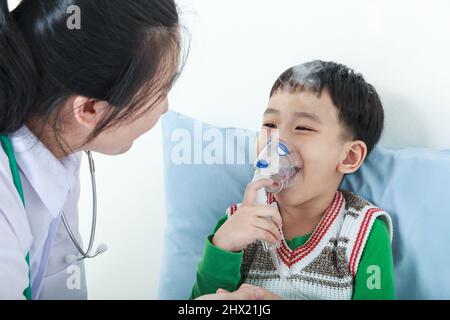 Glückliches Kind mit Atemwegserkrankung, das von einem Arzt mit Inhalator unterstützt wurde. Kinderarzt kümmern asiatischen Jungen mit Asthma Probleme machen Inhala Stockfoto