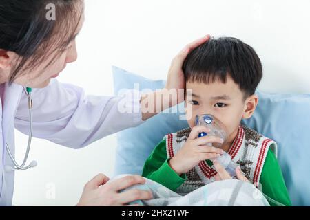 Trauriges Kind mit Atemwegserkrankungen, das von einem Arzt mit Inhalator unterstützt wurde. Kinderarzt kümmern asiatischen Jungen mit Asthma Probleme machen inhalati Stockfoto