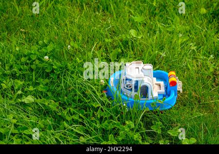 Weiß-blaues Bootsspielzeug an Land auf grünem Gras Rasen Kleeblatt Stockfoto